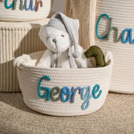 A basket with the name George holding a teddy and a toy dinosaur
