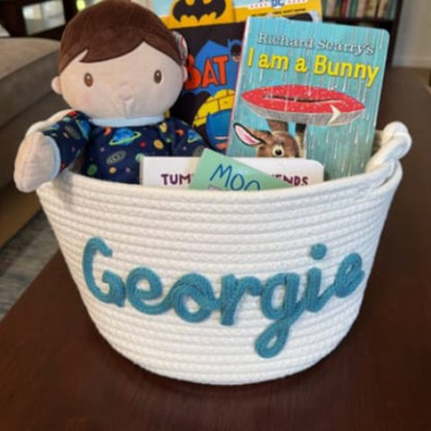 A basket with the name Georgie holding books and a doll