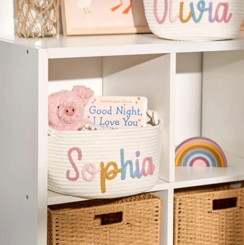 A basket with the name Sophia on a nursery shelf with a book and a toy pig